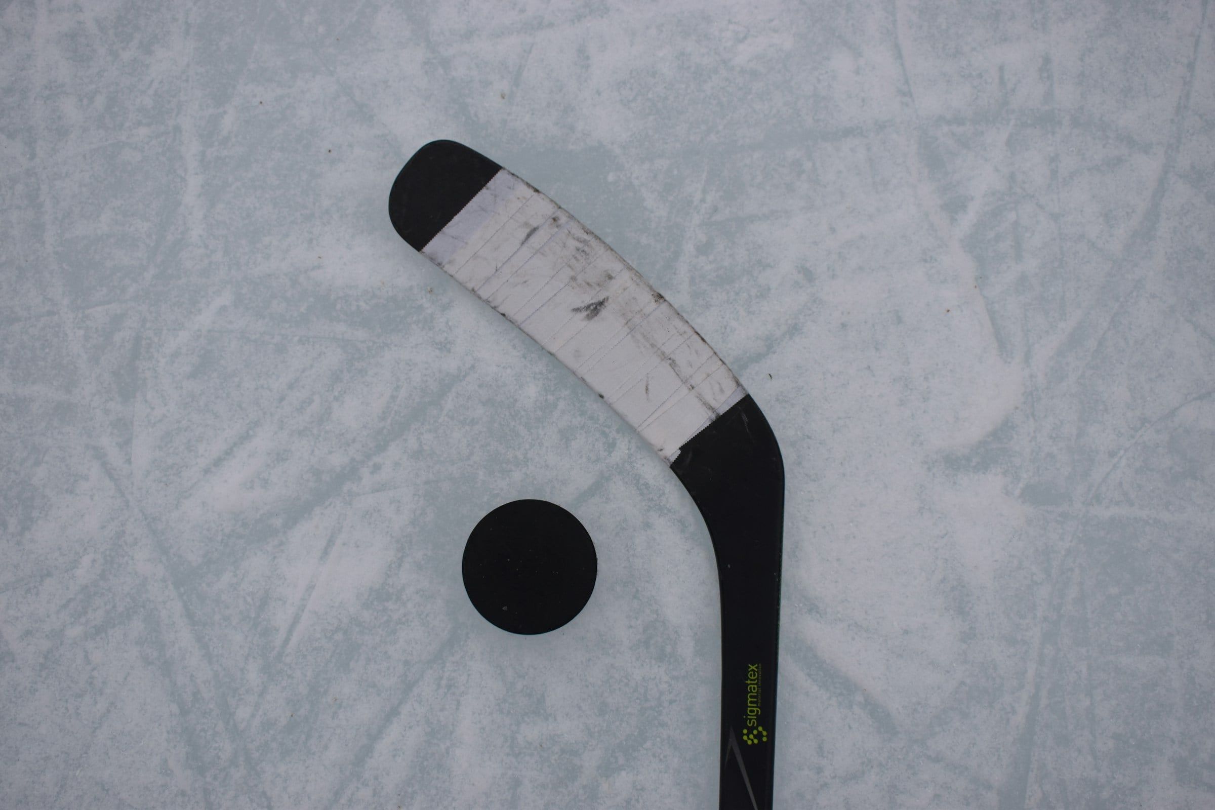 Bastone da hockey e disco nero appoggiati sul ghiaccio graffiato di una pista, ripresi dall'alto in luce naturale