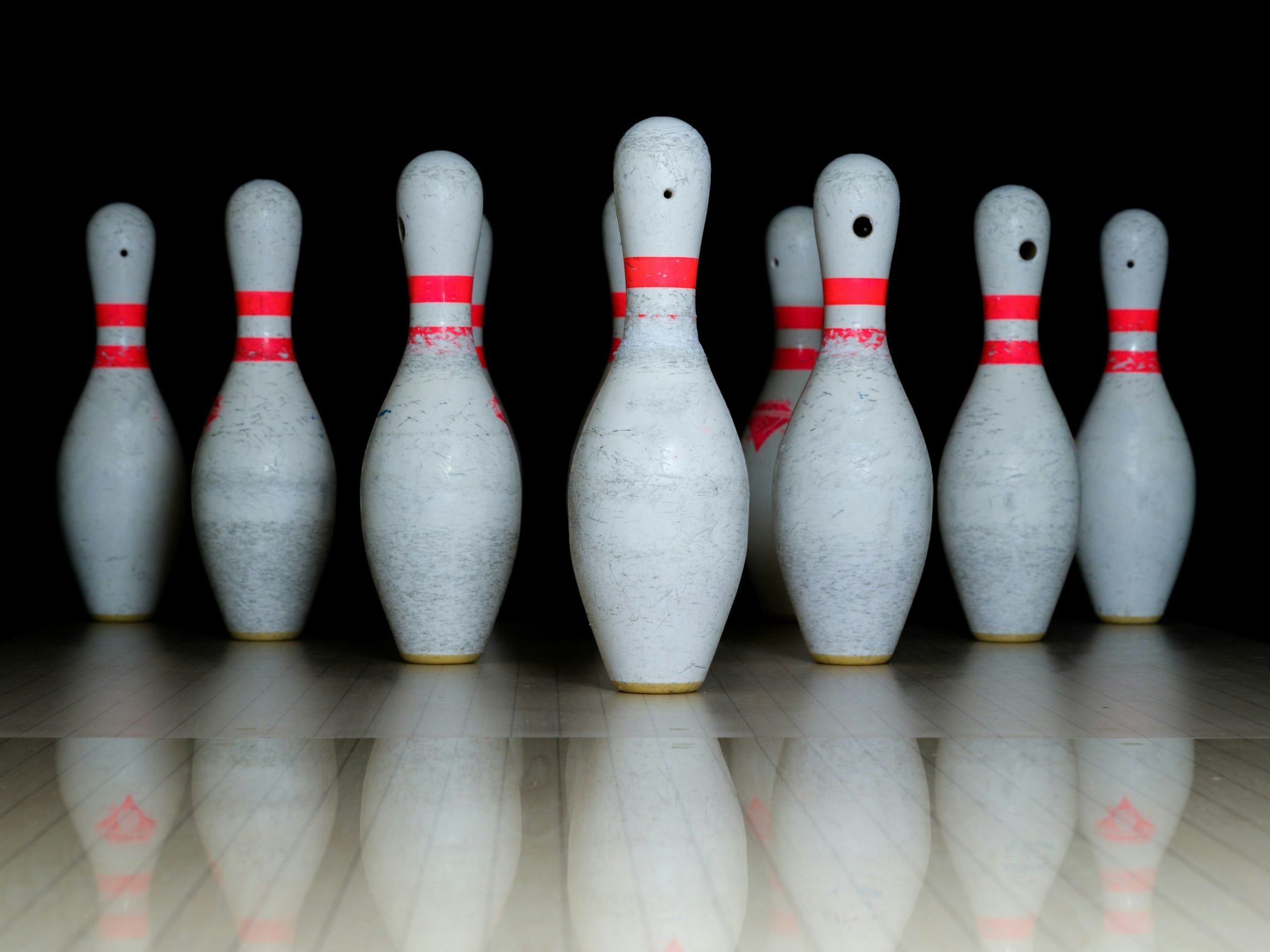 Birilli da bowling bianchi con le fasce rosse allineati sulla pista lucida, ripresi in primo piano su uno sfondo nero