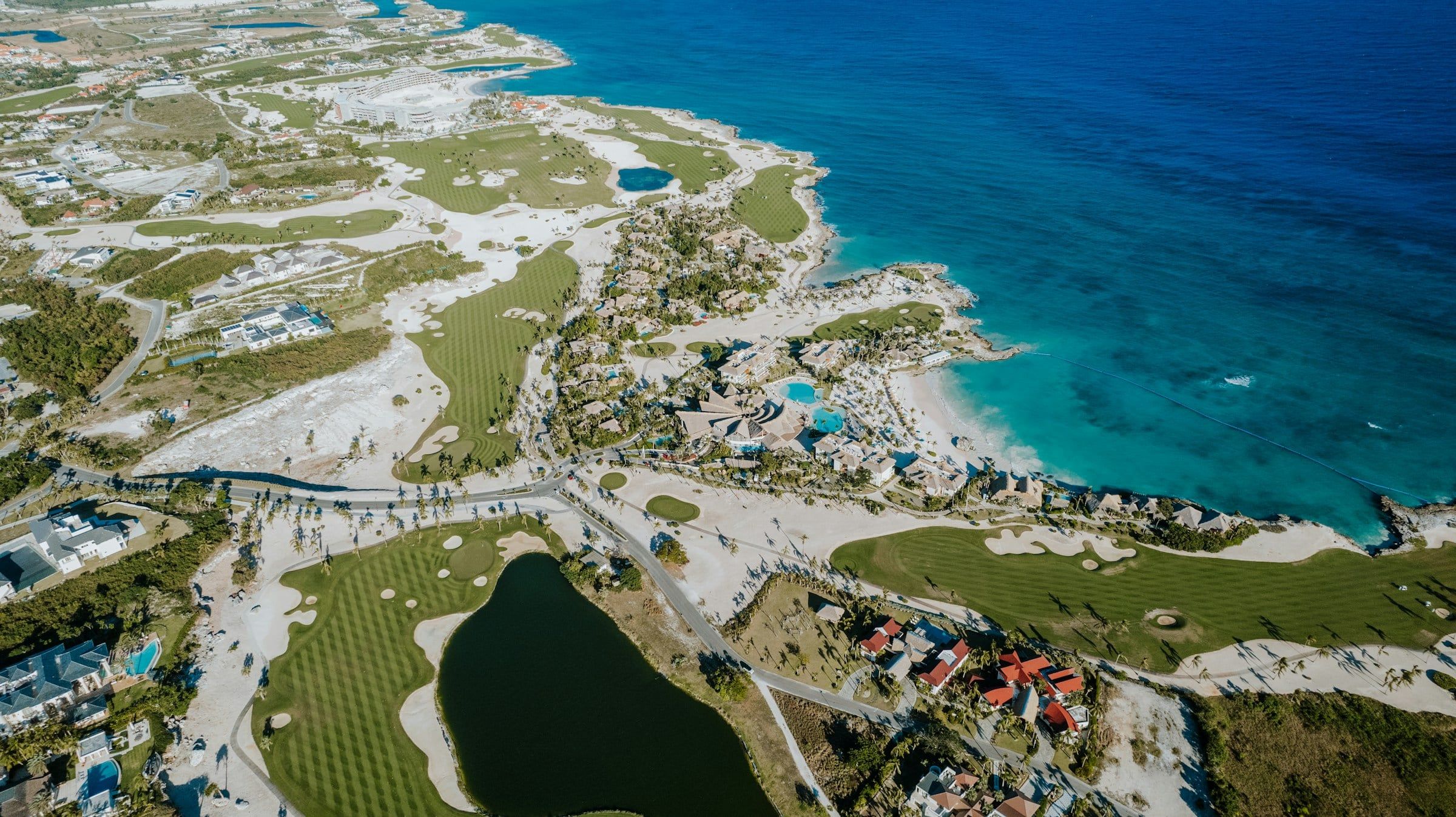 Vista aerea di un campo da golf affacciato sul mare turchese, con i green che seguono la costa rocciosa e un piccolo lago