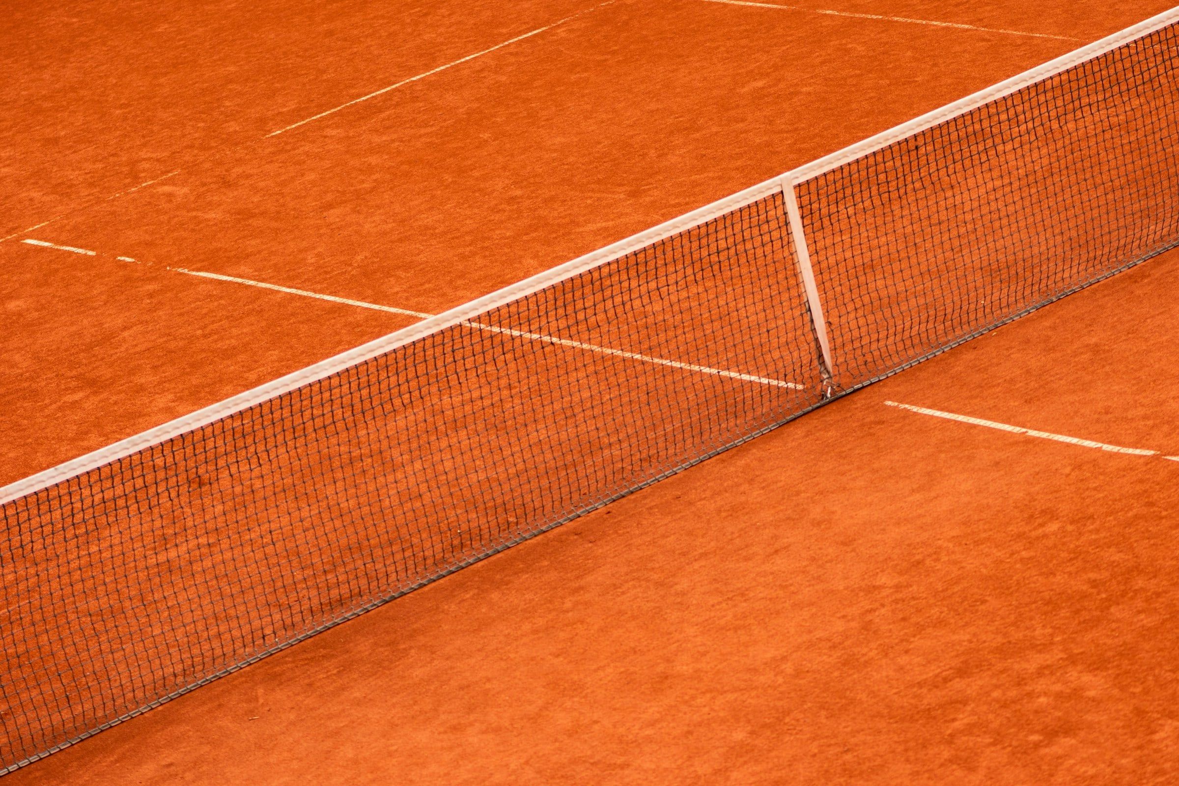 Campo da tennis in terra rossa ripreso dall'alto in diagonale, con la rete tesa al centro e le linee bianche ben tracciate