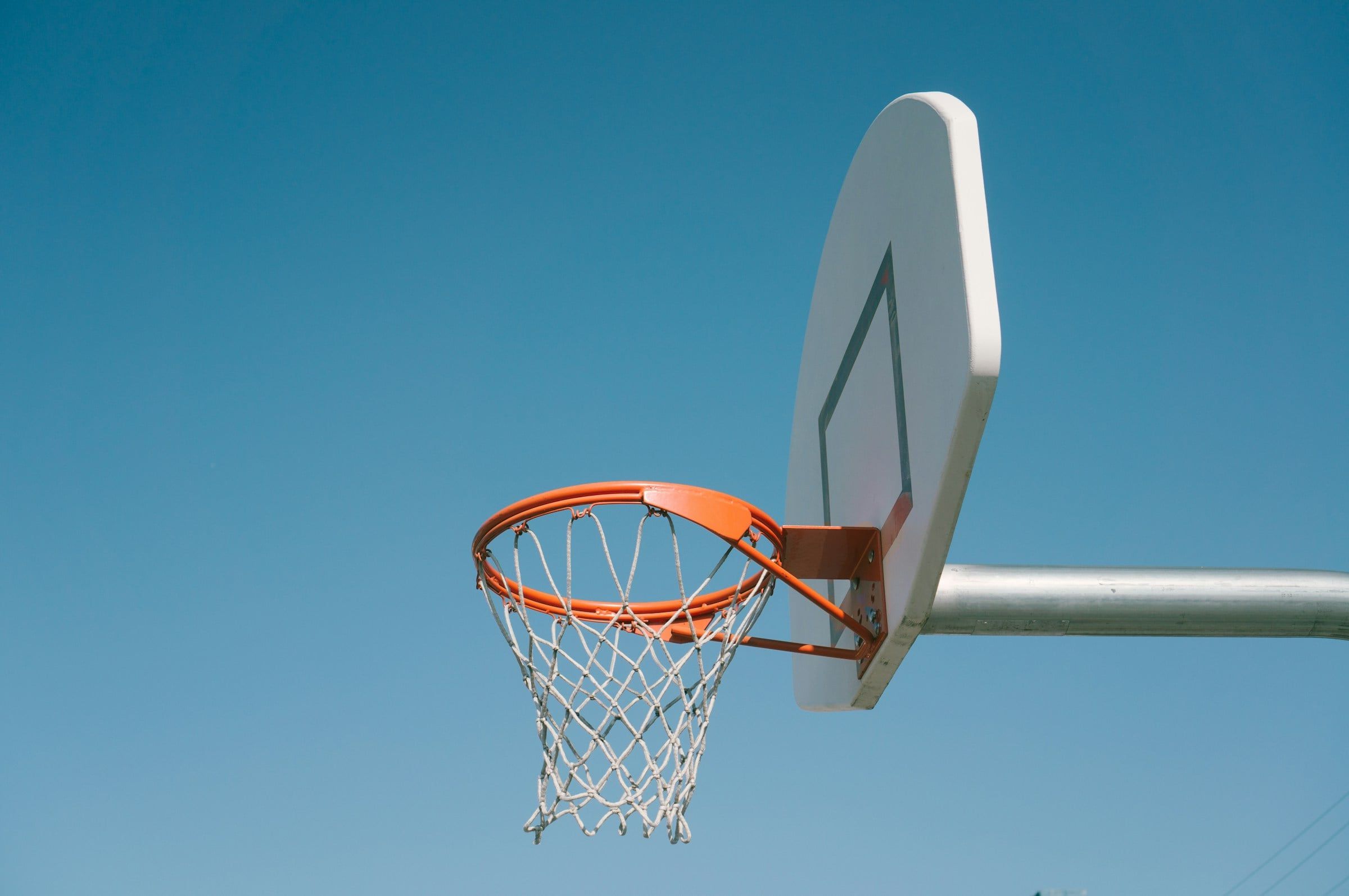 Canestro da basket all'aperto con il tabellone bianco e la retina, ripreso dal basso contro un cielo azzurro e limpido