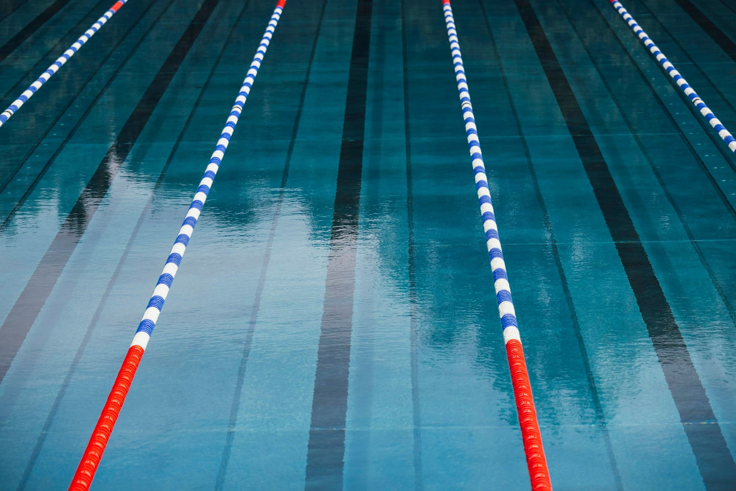 Corsie di una piscina vuota separate dai galleggianti rossi e blu, con l'acqua azzurra che riflette le luci della vasca