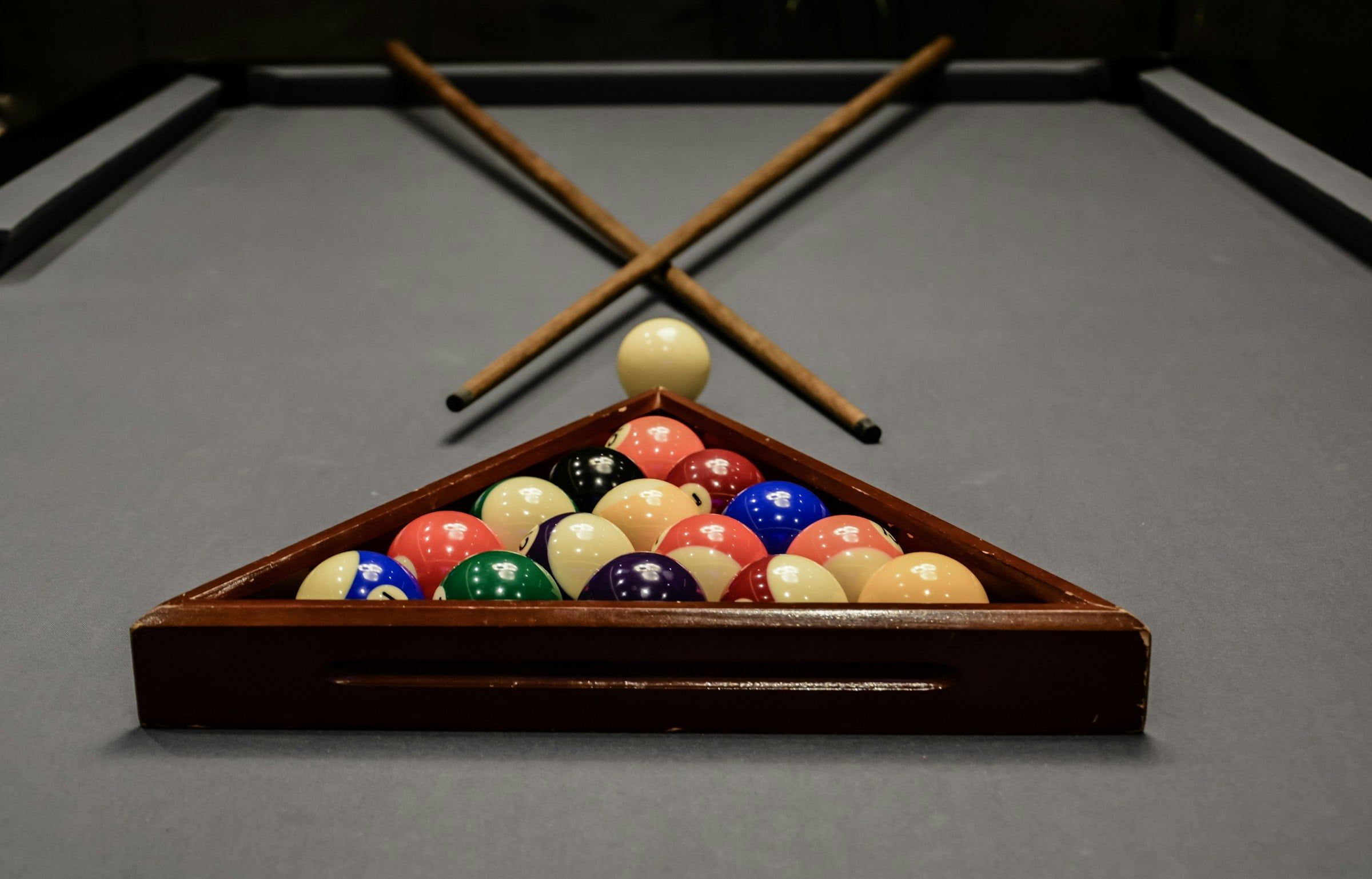 Palle da biliardo colorate raccolte nel triangolo di legno sul panno del tavolo, con due stecche incrociate appoggiate sopra