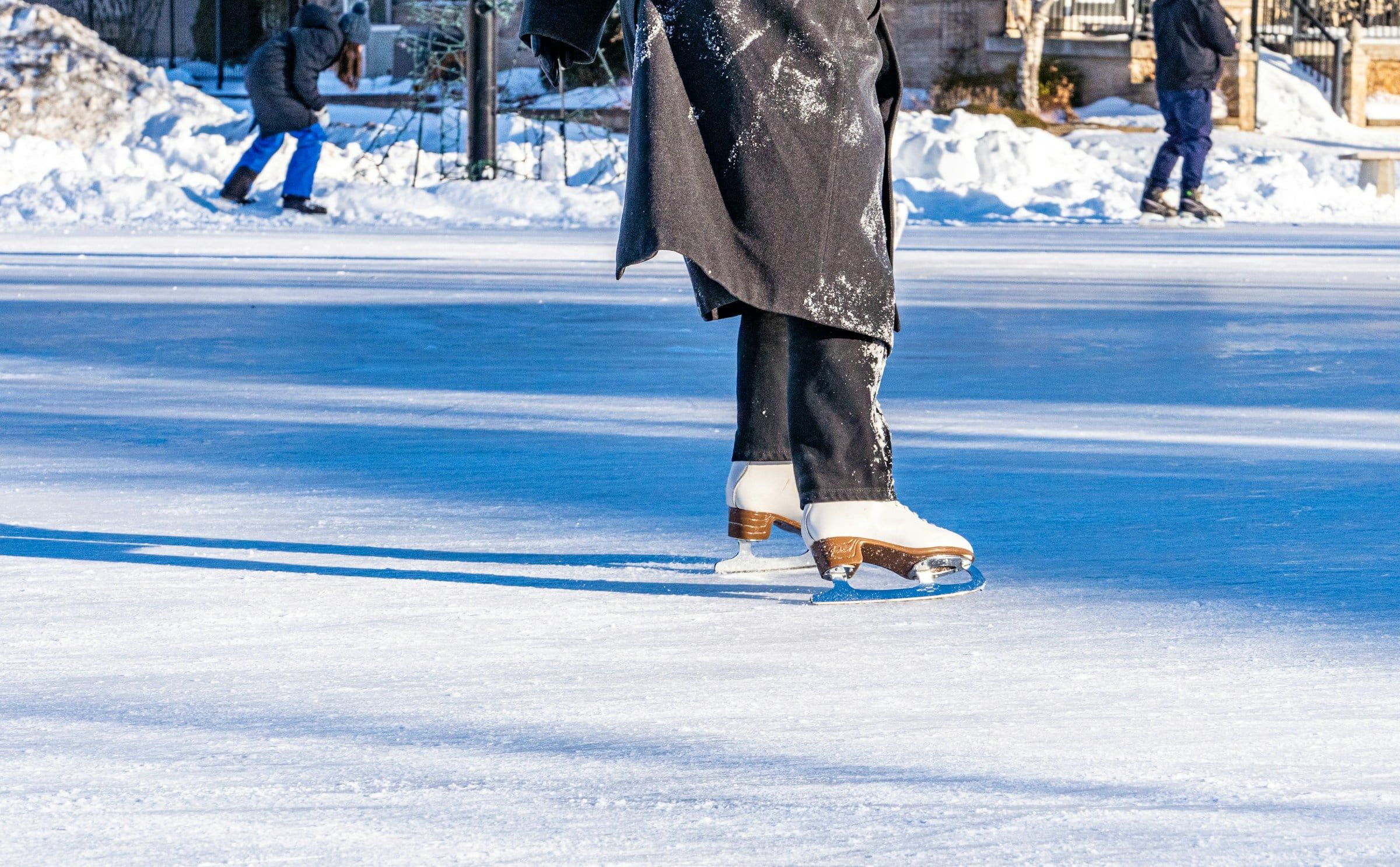 Pattini da ghiaccio bianchi in movimento su una pista all'aperto, tra riflessi azzurri sul ghiaccio e la neve ai bordi