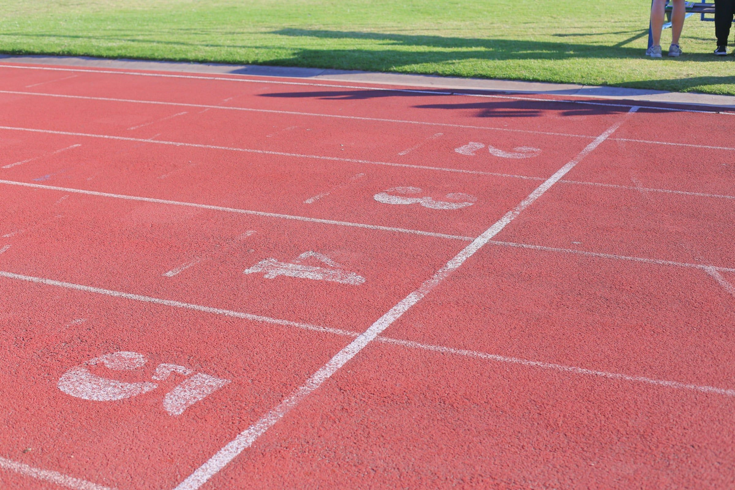 Corsie di una pista di atletica in tartan rosso, con le linee bianche e i numeri delle corsie dipinti a terra accanto al prato