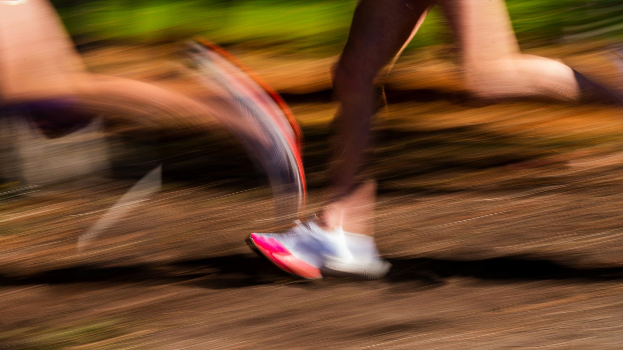 Gambe di un runner in corsa riprese con l'effetto mosso, con le scarpe da running che sfiorano il terreno in piena velocità