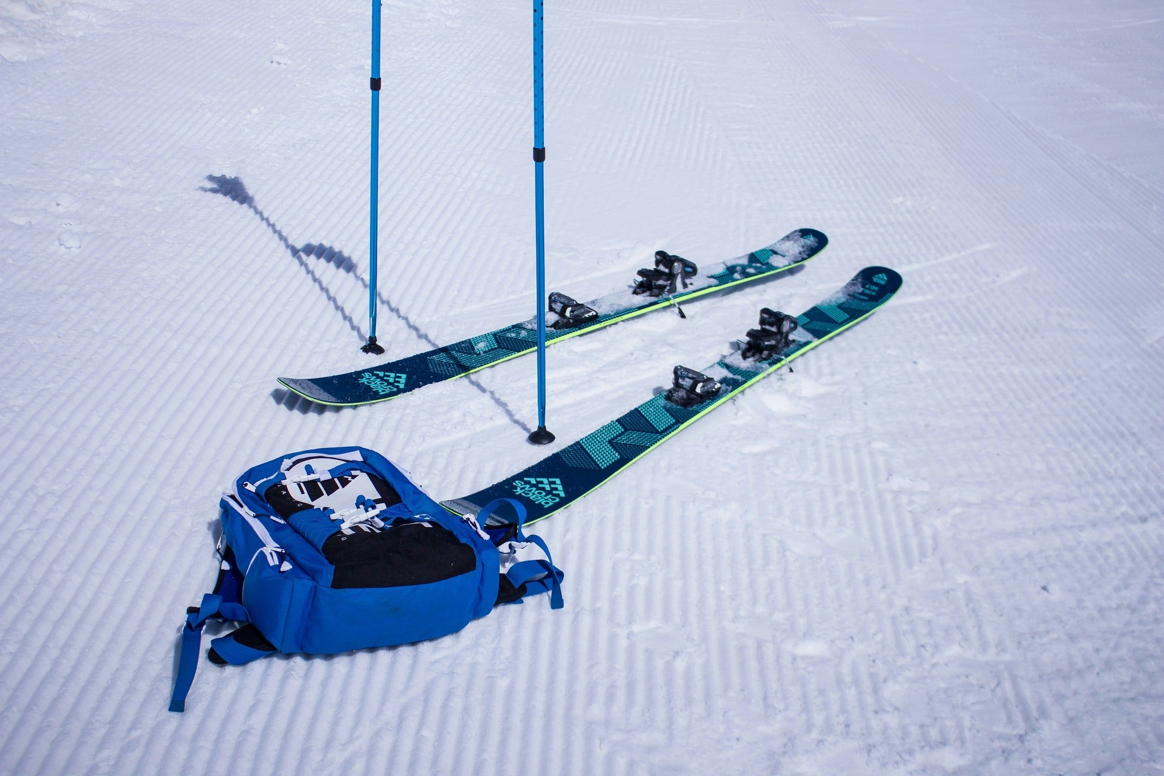 Sci, bastoncini e uno zaino blu appoggiati sulla neve battuta di una pista, pronti per una giornata in montagna