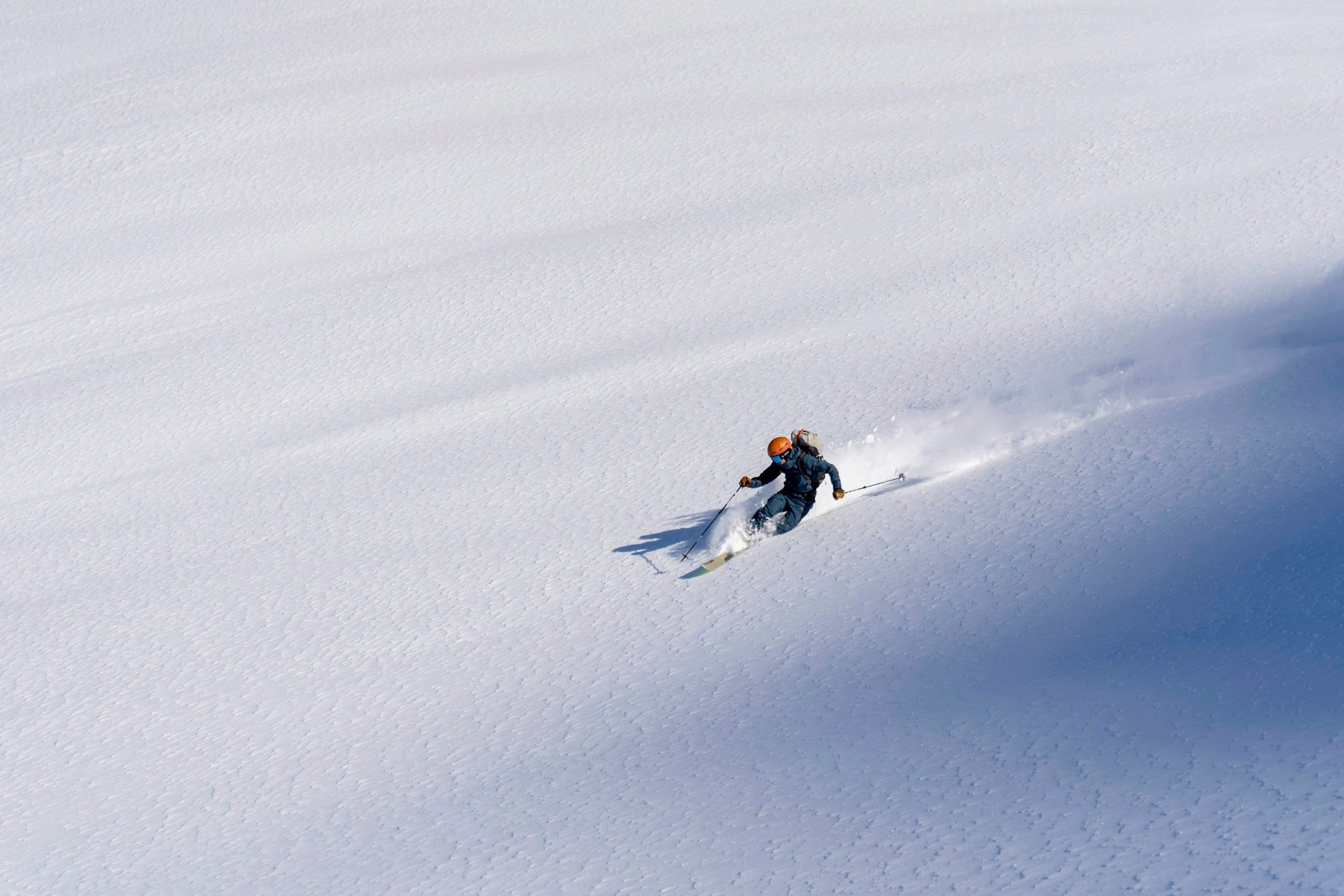 Sciatore lontano che scende in neve fresca su un pendio immacolato, lasciando dietro di sé una scia di polvere bianca