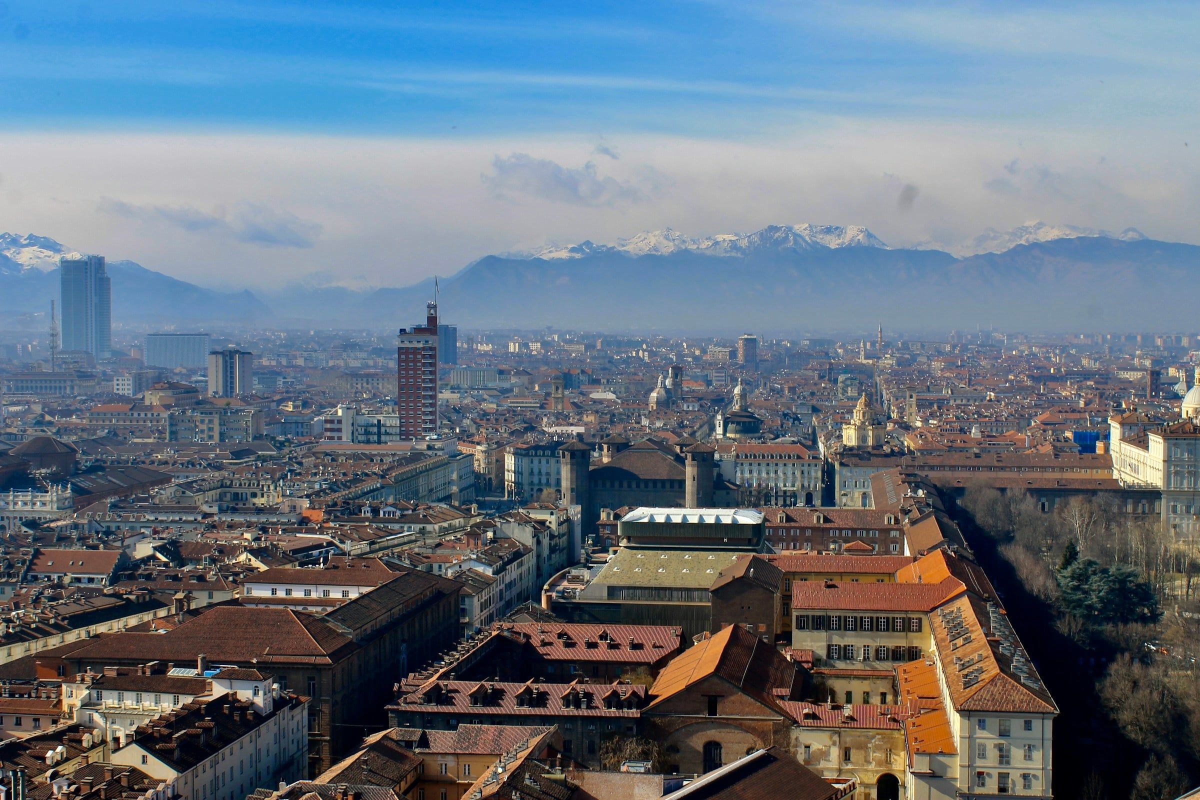 Panorama dei tetti di Torino visti dall'alto in una giornata limpida, con i palazzi del centro e le Alpi innevate sullo sfondo